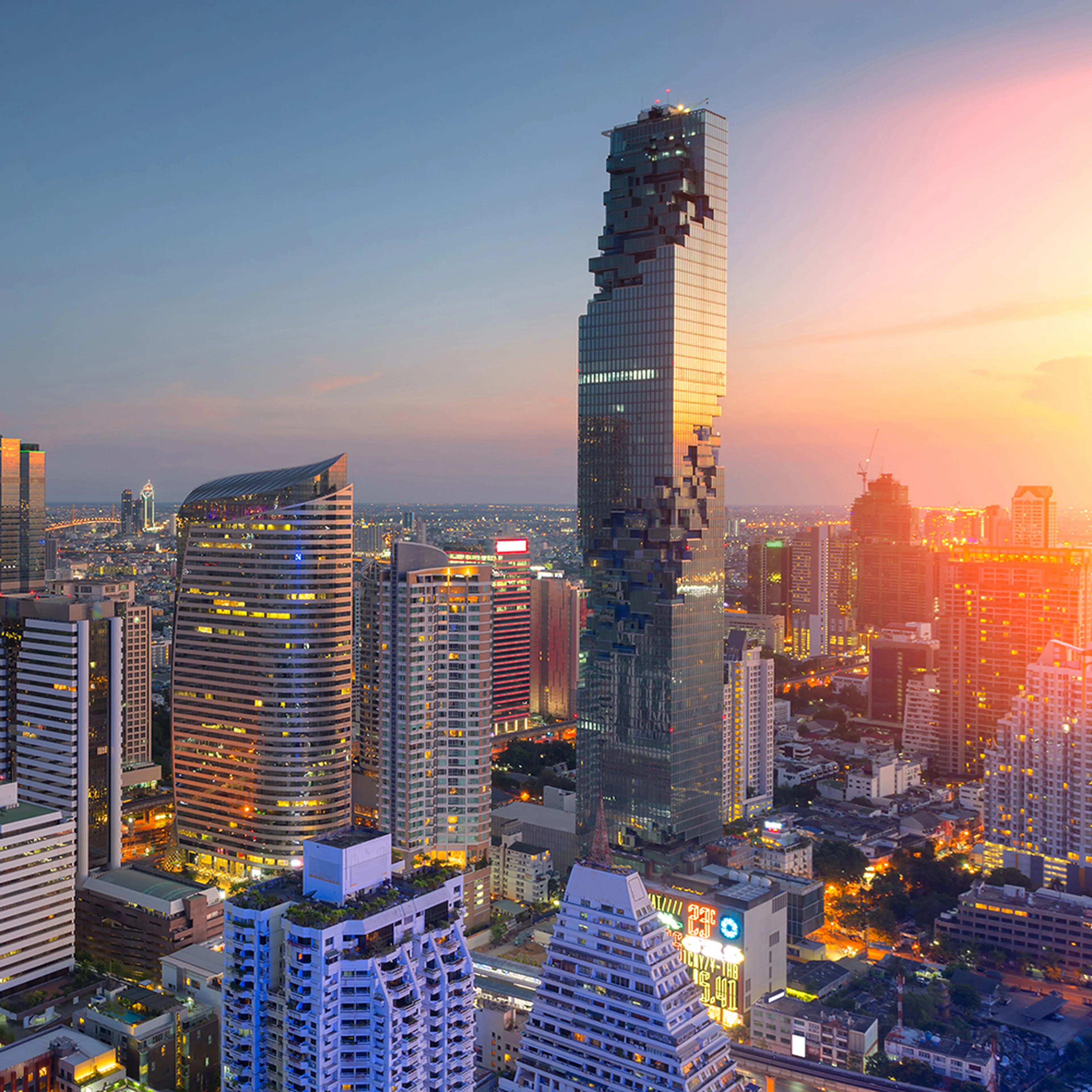 City skyline at sunset with a distinctive pixelated skyscraper and surrounding modern buildings, under a colorful sky.