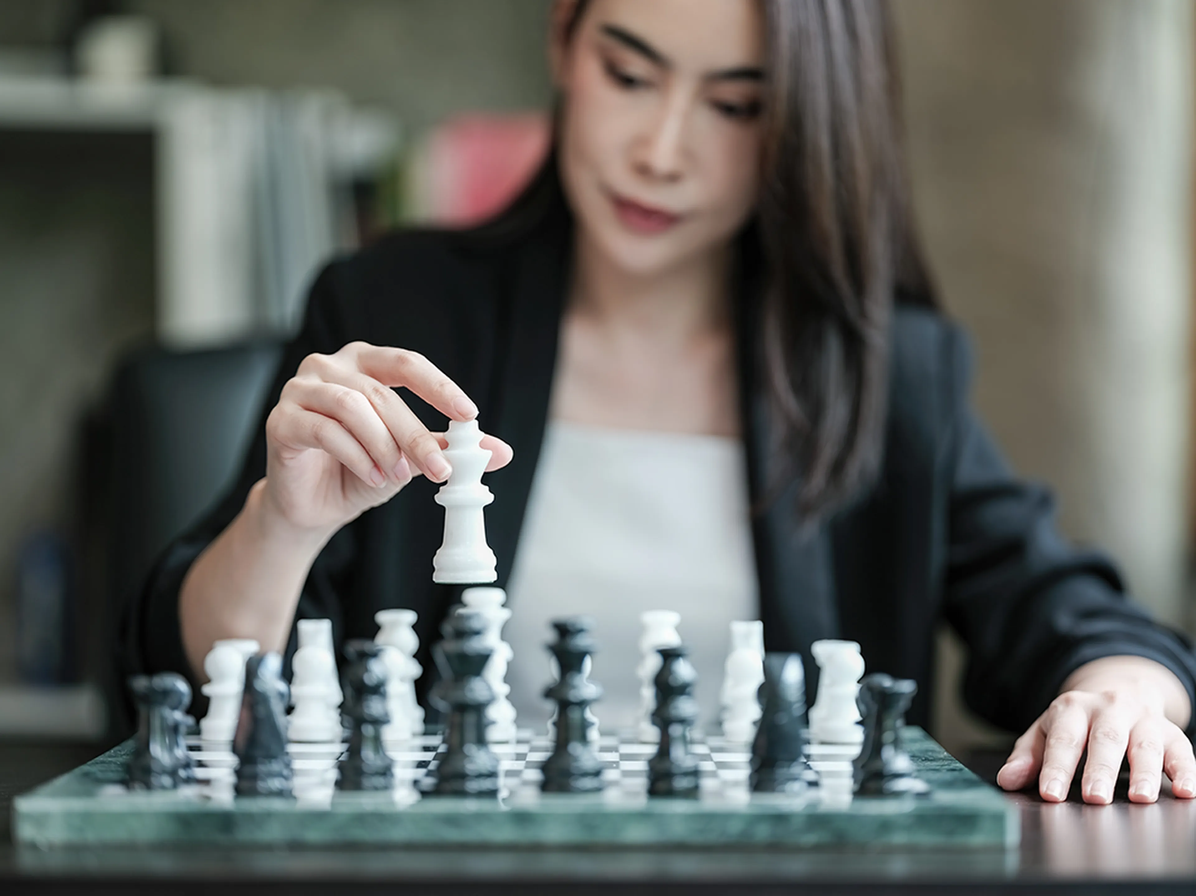 Woman playing chess, focusing on moving a white piece on a glass chessboard.